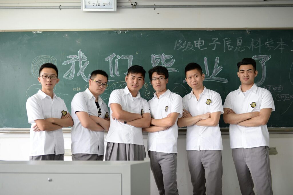 Group of male students standing confidently in classroom setting with chalkboard background.