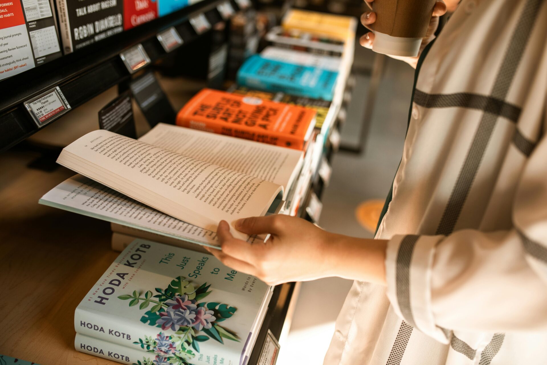 Person reading a book indoors with a coffee cup in a bookstore setting.