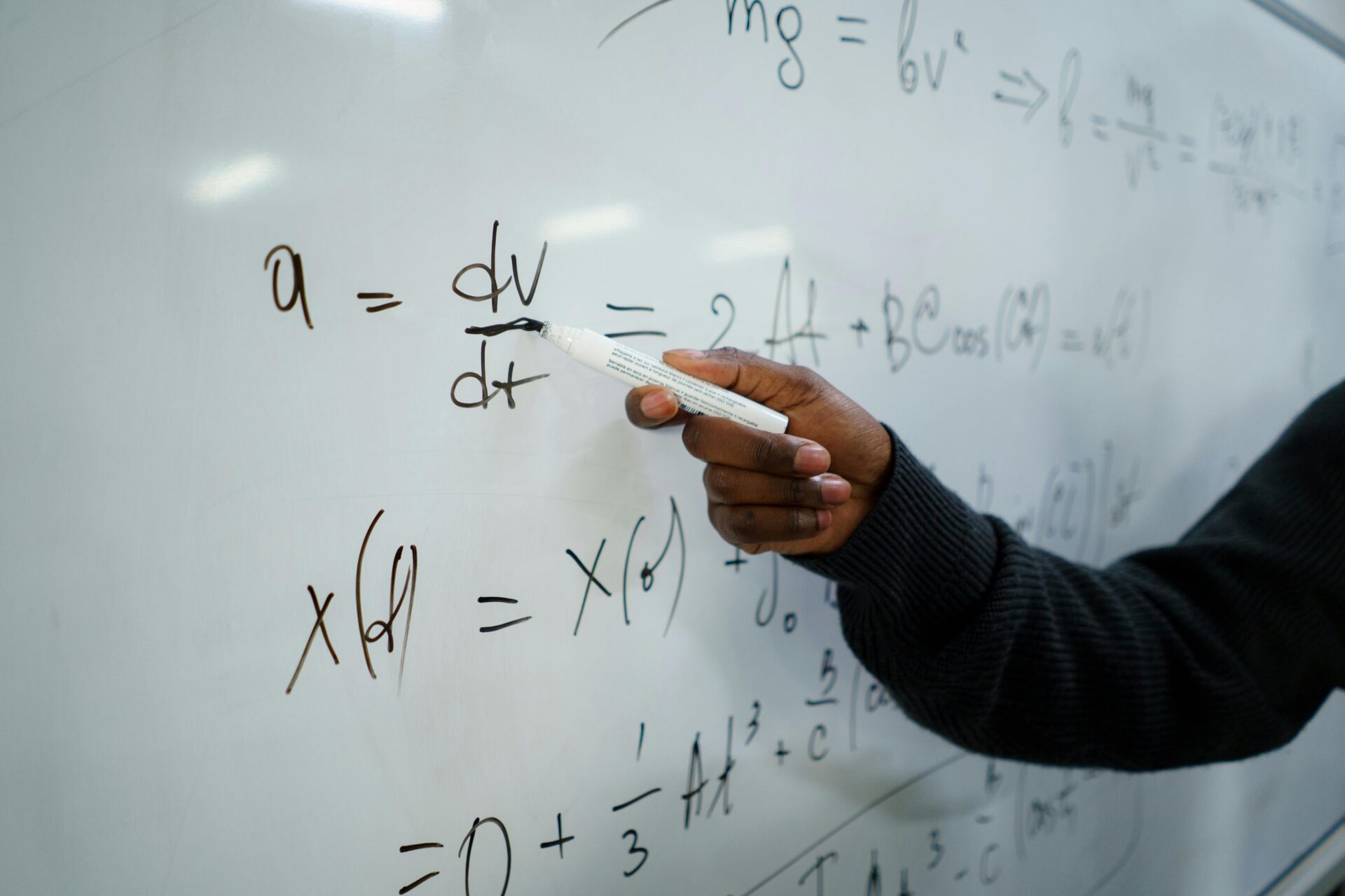 Close-up of hand writing equations on a whiteboard in a classroom setting.
