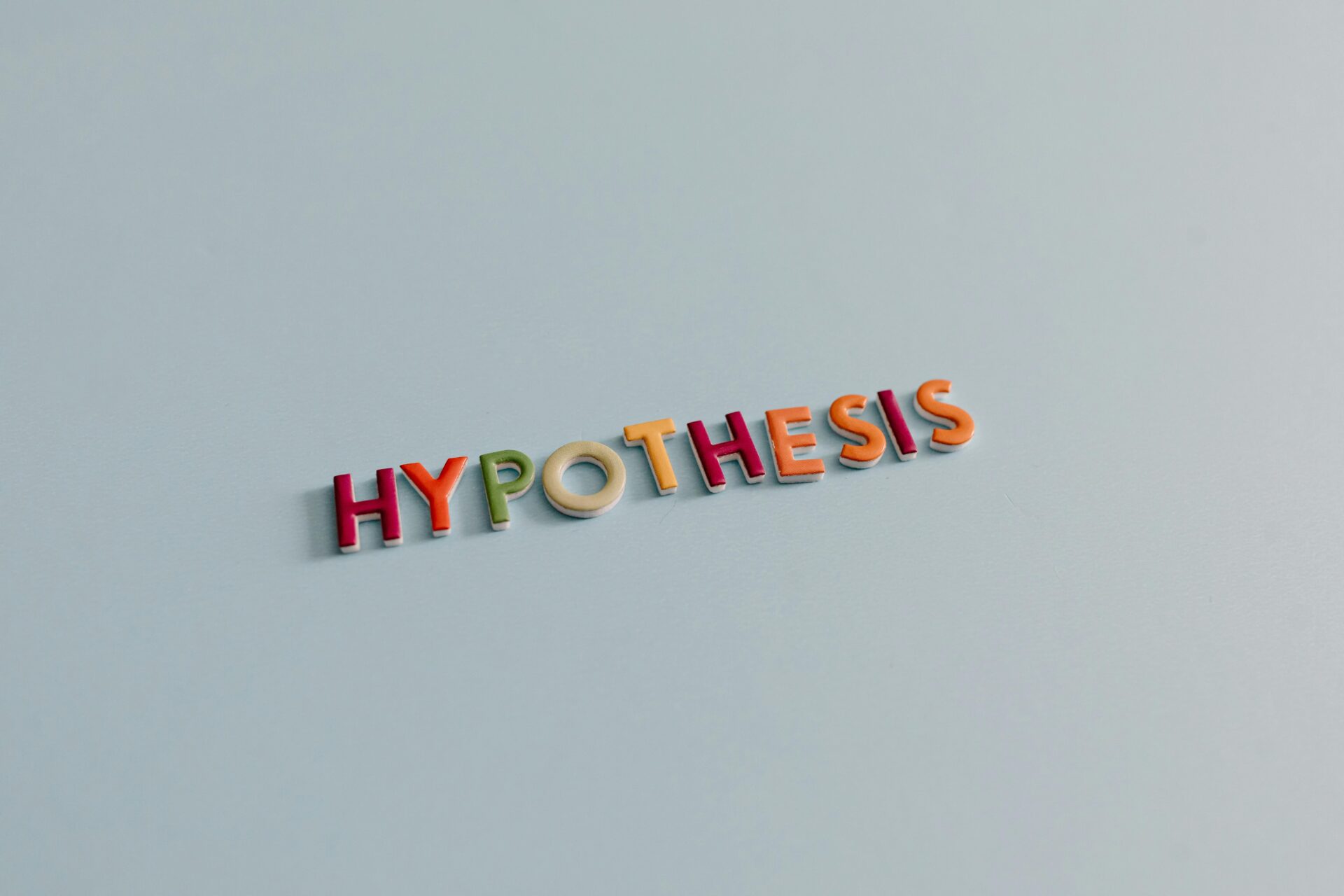 Multicolored letters spell 'HYPOTHESIS' on a light blue surface, conveying research and creativity.