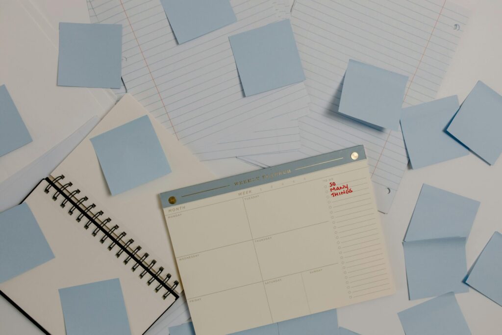 Top view of a desk with planner, sticky notes, and lined papers for organization.