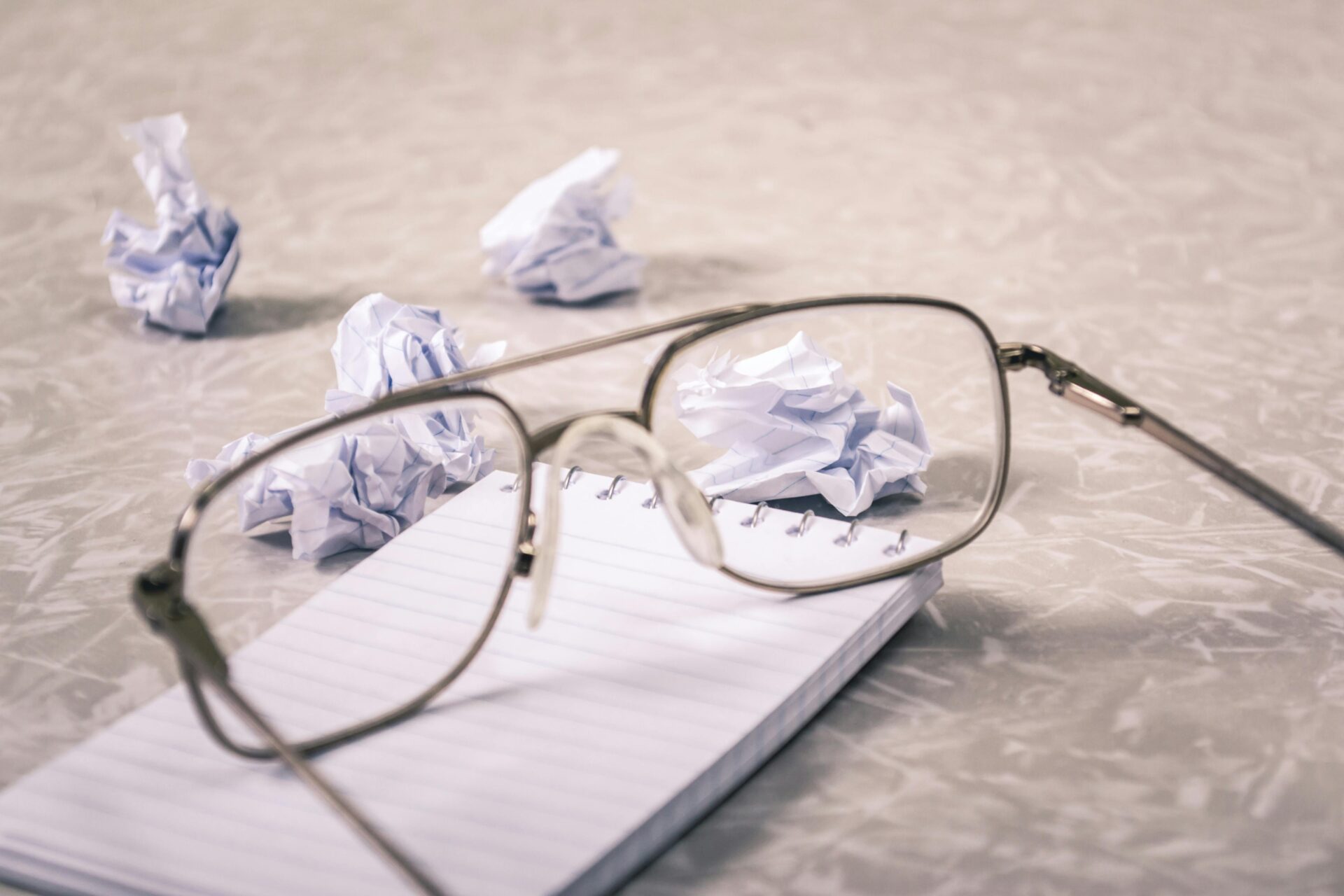 Eyeglasses and crumpled paper on notepad, symbolizing creative brainstorming process.